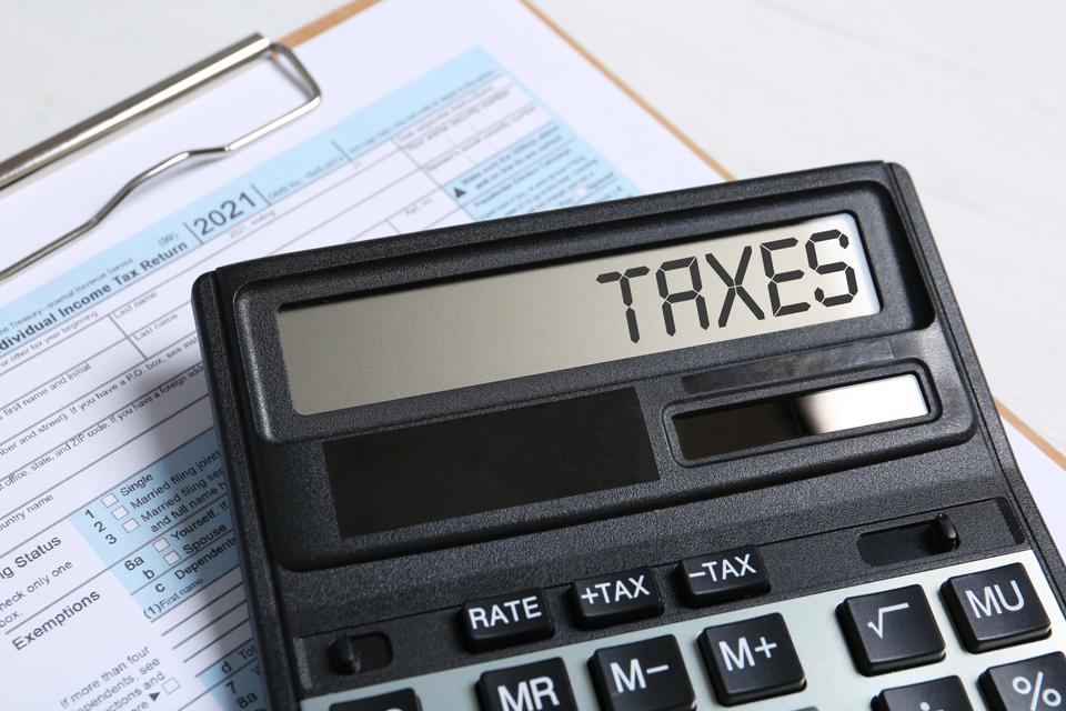 Calculator with word Taxes and document on table, closeup